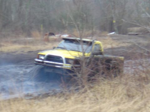 1987 Suzuki Samurai - A yellow pickup truck navigates through a muddy, off-road terrain.