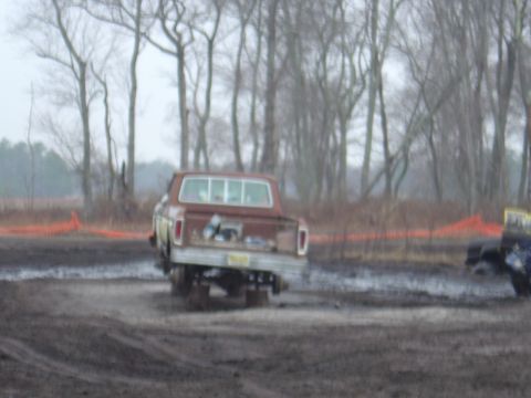 1987 Suzuki Samurai - A brown pickup truck navigates through a muddy terrain with trees in the background.