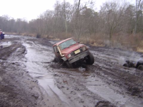 1987 Suzuki Samurai - Red 1987 Suzuki Samurai is stuck in deep mud on a trail, with another vehicle in the background.