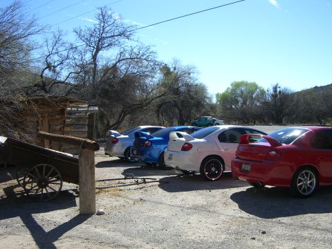 1996 Ford Probe - Multiple Dodge Neon SRT-4s are parked in a lot with a rustic building in the foreground.