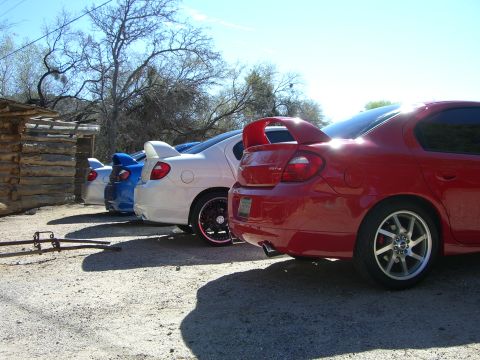 1996 Ford Probe - A line of sedans, including a red one with a prominent spoiler, are parked outdoors.