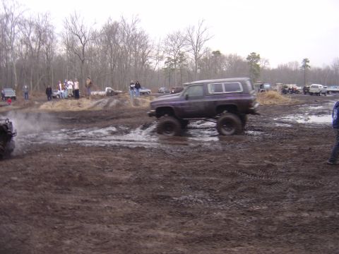 1987 Suzuki Samurai - A lifted SUV navigates a muddy track while spectators observe the off-road event.