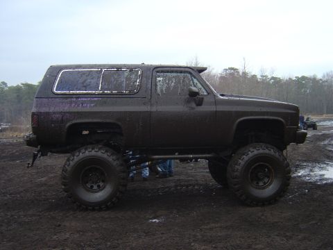 1987 Suzuki Samurai - Mud-covered SUV with oversized tires sits in a muddy outdoor area.