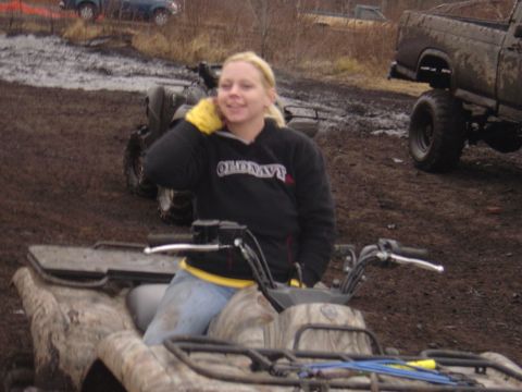 1987 Suzuki Samurai - A woman sits on a camouflage ATV in a muddy outdoor setting, with a lifted truck and other ATVs visible in the background.