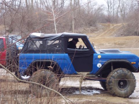 1974 Ford Bronco - A blue 1974 Ford Bronco navigates a muddy off-road course with another vehicle in the background.