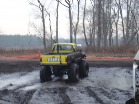 1987 Suzuki Samurai - A modified pickup truck with oversized tires navigates a muddy terrain, displaying 'DEERE' on its tailgate.
