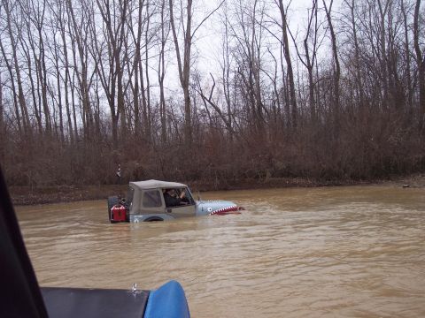 1974 Ford Bronco - A Jeep Wrangler with shark teeth painted on its grille navigates through murky water surrounded by bare trees.