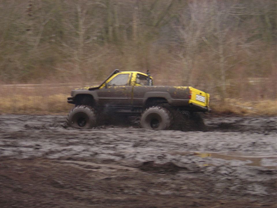 Yellow and dark modified pickup truck with large tires driving through deep mud