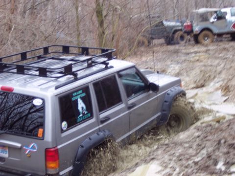 1974 Ford Bronco - Several off-road vehicles navigate a muddy trail, with one Jeep Cherokee XJ deeply stuck in the mire.