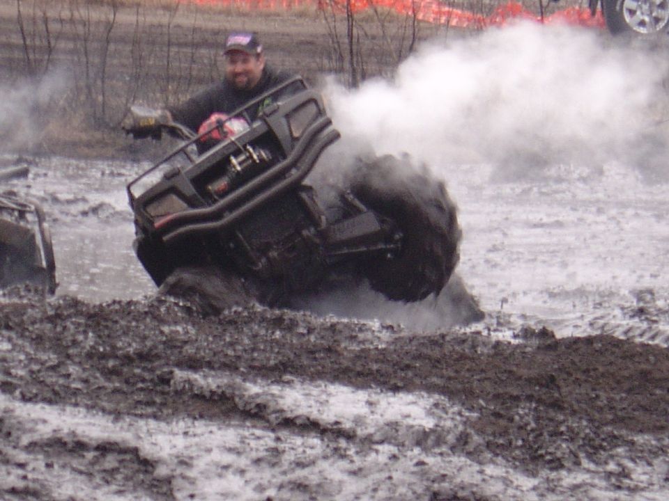 ATV stuck in mud with driver looking at camera. Another ATV is partially visible to the left