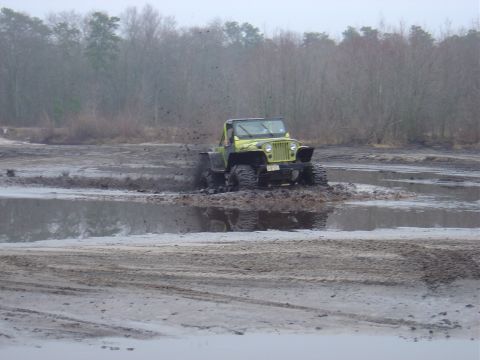 1987 Suzuki Samurai - This Jeep is navigating a muddy off-road course, with trees in the background.