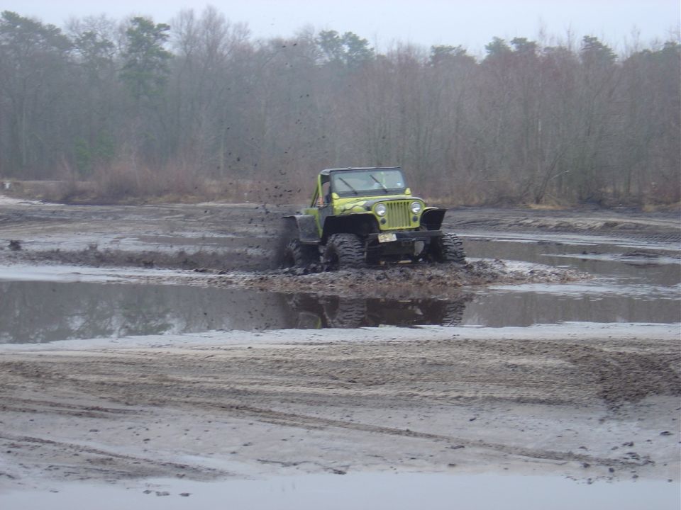 Jeep Wrangler driving through mud and water, kicking up spray