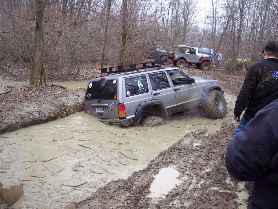 Silver Jeep Cherokee XJ stuck in a muddy ditch with other Jeeps nearby