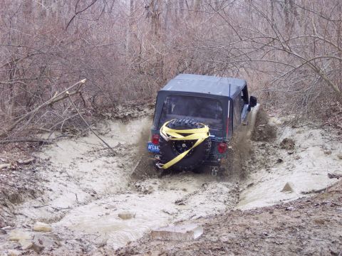 1974 Ford Bronco - A black Jeep Wrangler navigates a muddy off-road trail, kicking up water and mud.