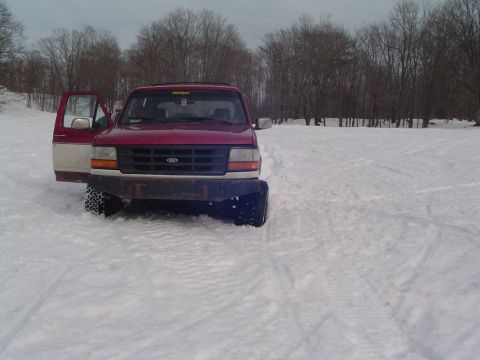 1994 Ford Bronco - A red and white Ford Bronco sits partially submerged in snow with its driver's door ajar.