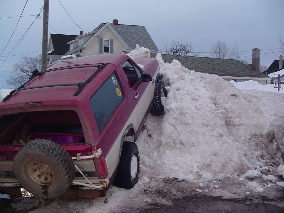 1994 Ford Bronco partially buried in a large snowbank on a street