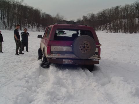 1994 Ford Bronco - A red Ford Bronco is stuck in deep snow with several people observing the situation.