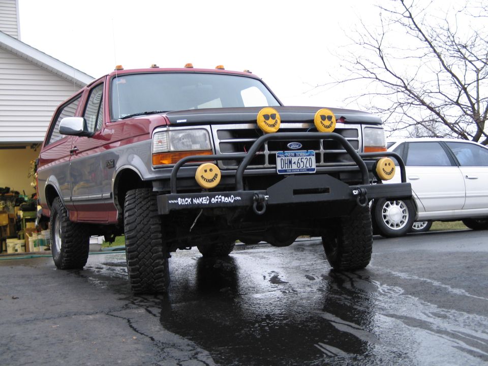 Red and grey Ford Bronco with a black bull bar, yellow smiley face lights, and "BUCK NAKED OFFROAD" text