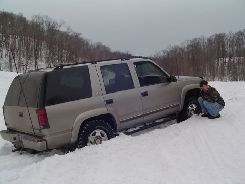 1994 Ford Bronco - A silver SUV is stuck in deep snow, with a person checking the front wheel.