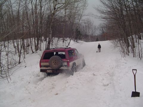 1994 Ford Bronco - Ford Bronco struggling through a snow-covered path in a wooded area, with a person and shovels nearby.