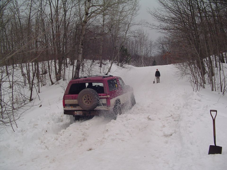1994 Ford Bronco stuck in deep snow on a wooded trail, spare tire mounted on rear door
