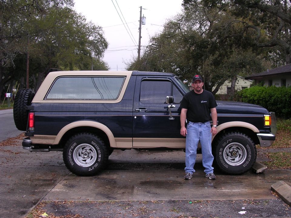 1988 Ford Bronco with a man standing next to it, side view. Dark blue and tan paint, spare tire on the rear