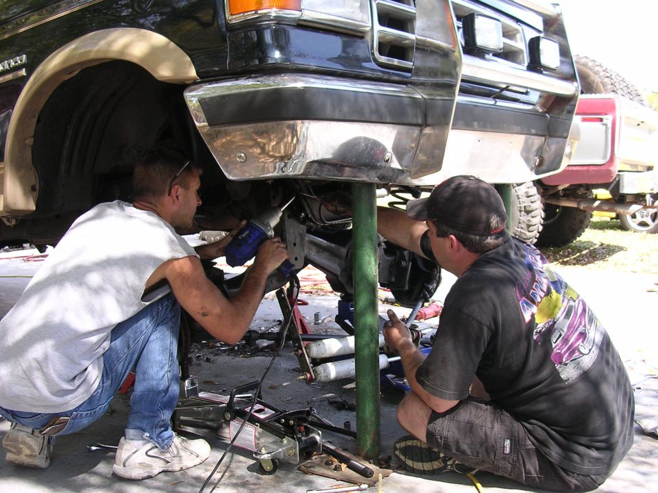 Truck front end being worked on by two men, with another red truck in the background
