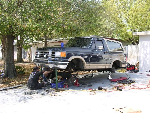 1988 Ford Bronco - Mechanics work on a dark blue 1988 Ford Bronco that is raised on a lift.
