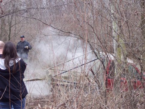 1974 Ford Bronco - A red vehicle is seen in a wooded area with smoke billowing around it, as onlookers observe.