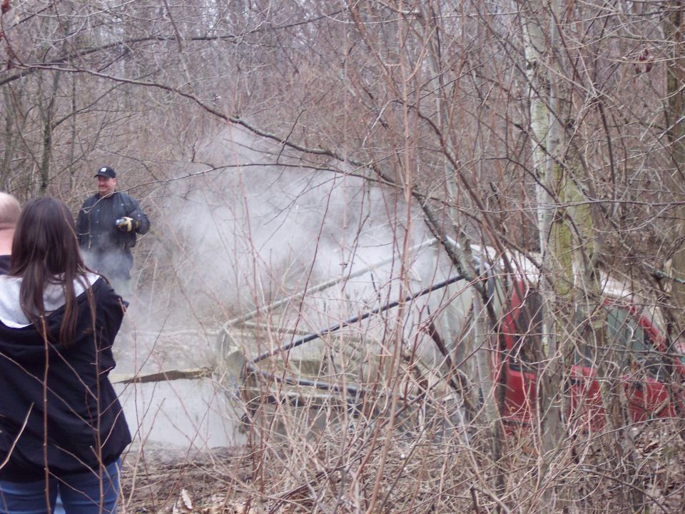 red SUV partially obscured by trees and smoke, with people watching