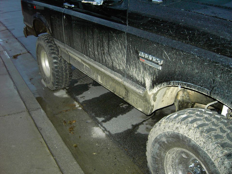Side view of a black lifted 1988 Ford Bronco with mud splatter and large tires
