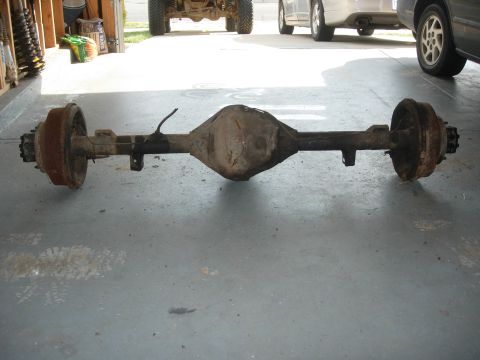 1995 Ford Bronco - A vehicle's rear axle assembly is shown, with other vehicles parked in the background.