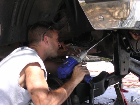 1988 Ford Bronco - A mechanic uses a blue impact wrench to work on the underside of a vehicle.