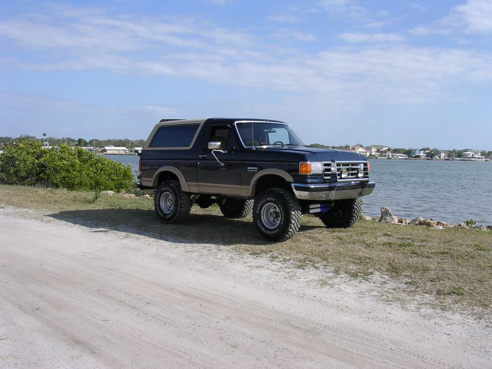 dark blue Ford Bronco parked by the water, lifted with large tires