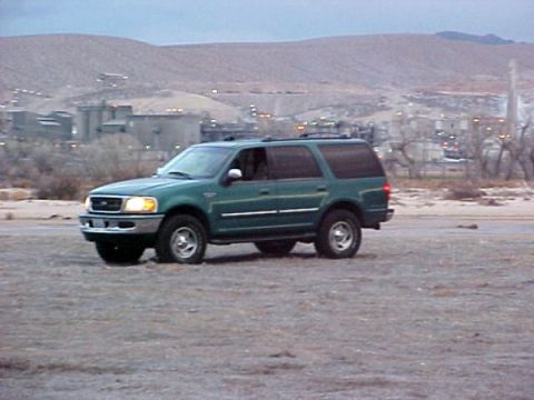 1997 Ford Expedition - A green 1997 Ford Expedition SUV is seen from a three-quarter front angle with an industrial landscape behind it.
