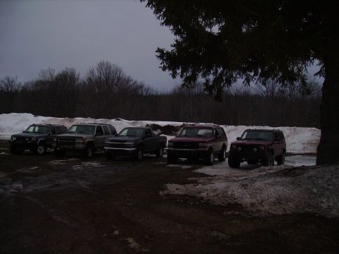 2000 Chevrolet Tahoe - A group of five SUVs and trucks are parked in a lot with snow on the ground, under the branches of a large tree.
