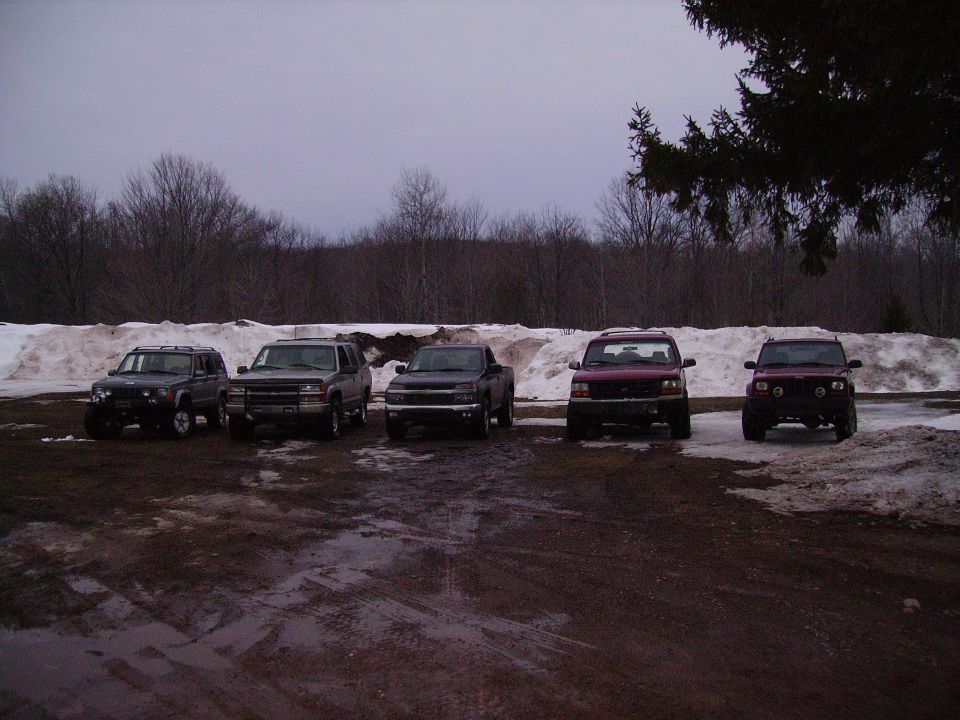 Five SUVs and trucks parked in a lot with snow in the background