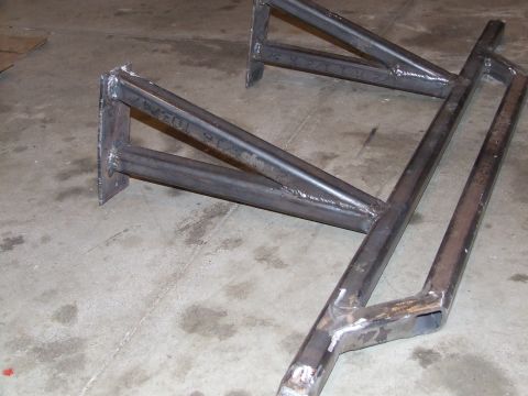 1986 Ford Bronco - Bare-steel fabricated tube rock sliders or nerf bars sitting on a shop's concrete floor, freshly MIG-welded with unpainted beads and chalk…