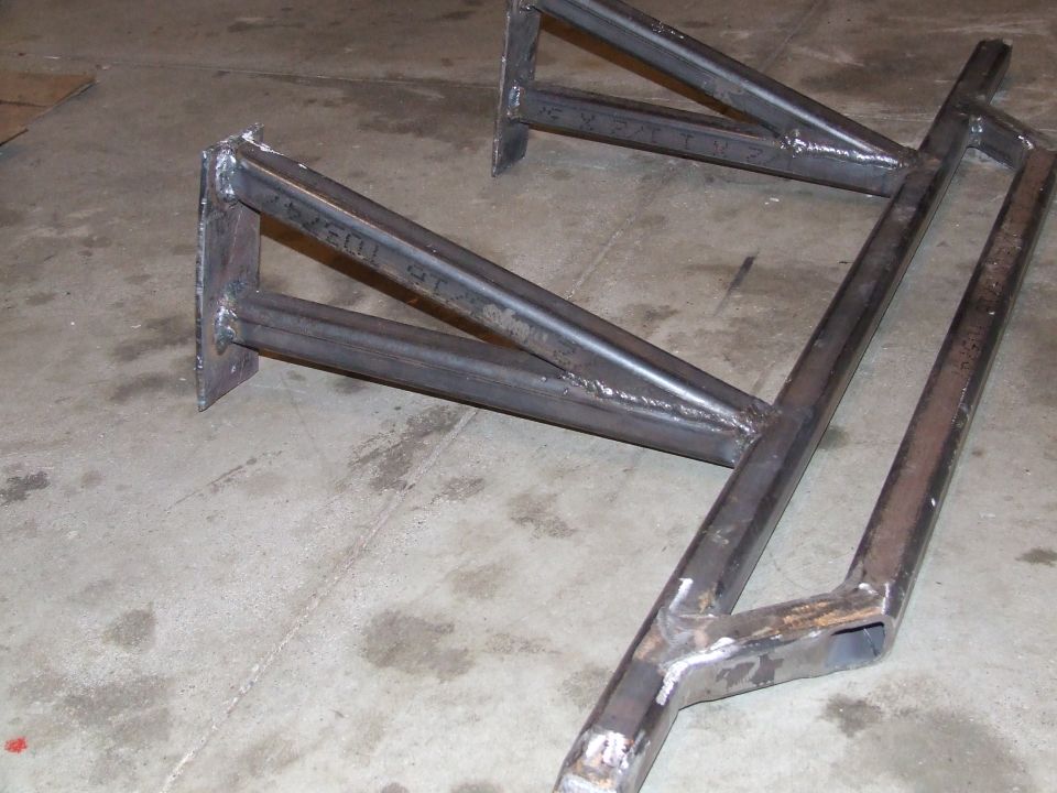 Bare welded steel tube rock sliders with mounting plates on a shop floor