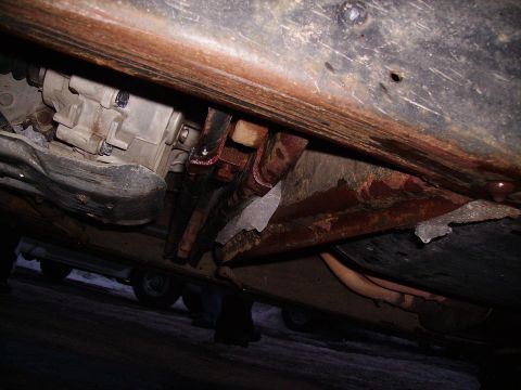 2000 Chevrolet Tahoe - The undercarriage of a vehicle displays significant rust and a view of its transmission, with another vehicle partially visible.