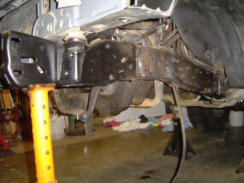 1989 Ford Bronco - Close-up view of vehicle frame and suspension components being worked on, with visible rust and fresh paint.