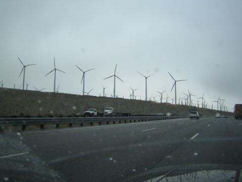 1990 Ford Bronco - Rows of wind turbines line a ridge above a multi-lane highway with passing vehicles under an overcast sky.