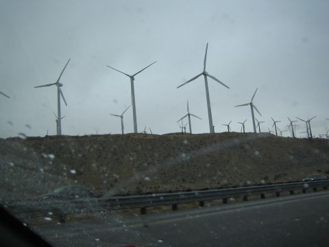 1990 Ford Bronco - cluster of wind turbines stands on a barren hillside, viewed through a rain-spotted windshield from a moving car.