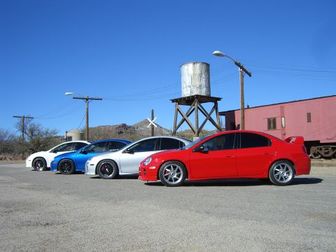 1996 Ford Probe - A lineup of four Dodge Neon SRT-4s are parked outdoors under a clear blue sky, with a vintage water tower and train car visible.