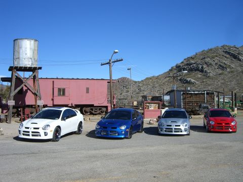 1996 Ford Probe - A quartet of Dodge Neon SRT-4s are lined up in front of a vintage train car and a water tower under a clear blue sky.