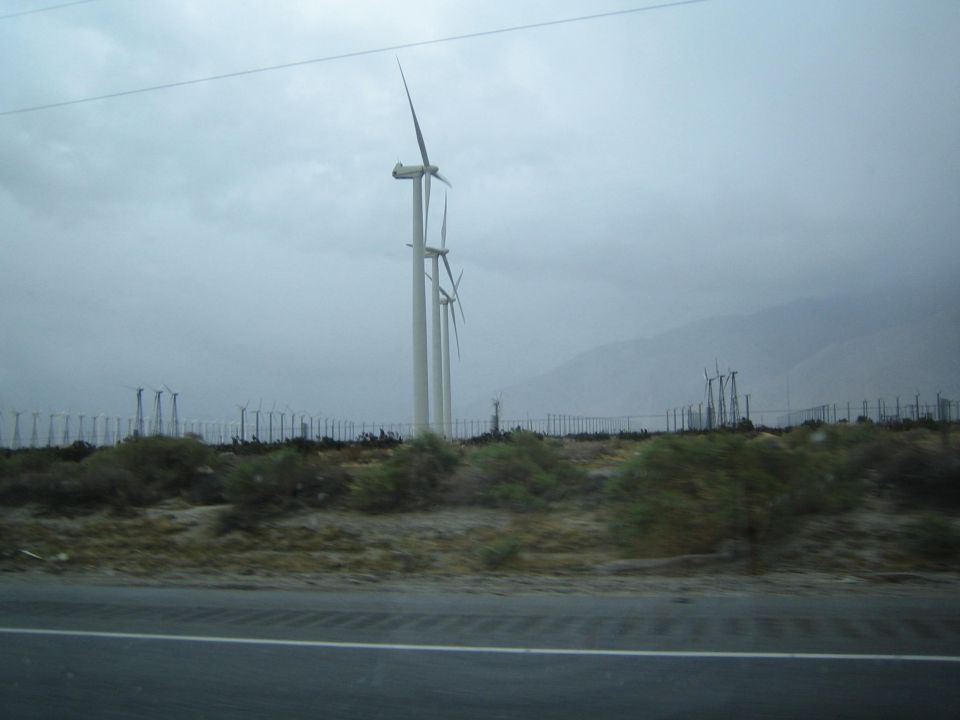 Tall wind turbines beside a desert highway with mountains in the background