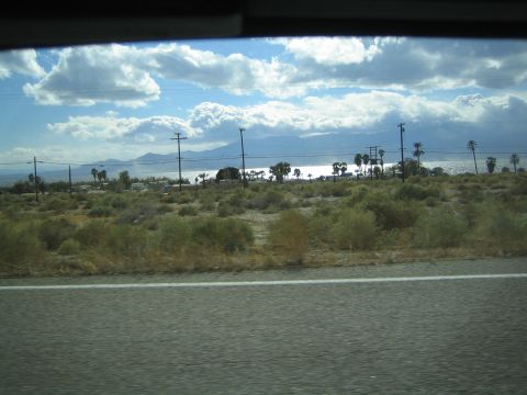 1990 Ford Bronco - Desert scrub and power poles frame a distant shimmering lake and mountains seen from a moving vehicle.