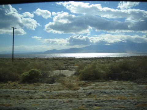 1990 Ford Bronco - lone power pole stands beside a shimmering desert lake backed by mountains under a partly cloudy sky.