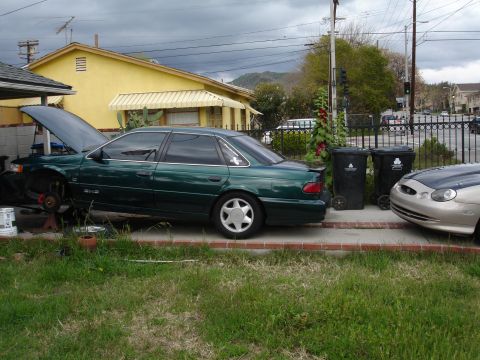 1993 Ford Taurus - A green 1993 Ford Taurus sedan is parked with its hood open, appearing to be under repair. A second vehicle is visible to the right.