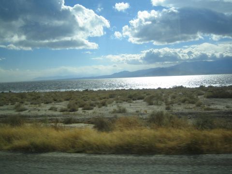1990 Ford Bronco - band of golden grass borders the road as sunlight glints off a desert lake backed by mountains.